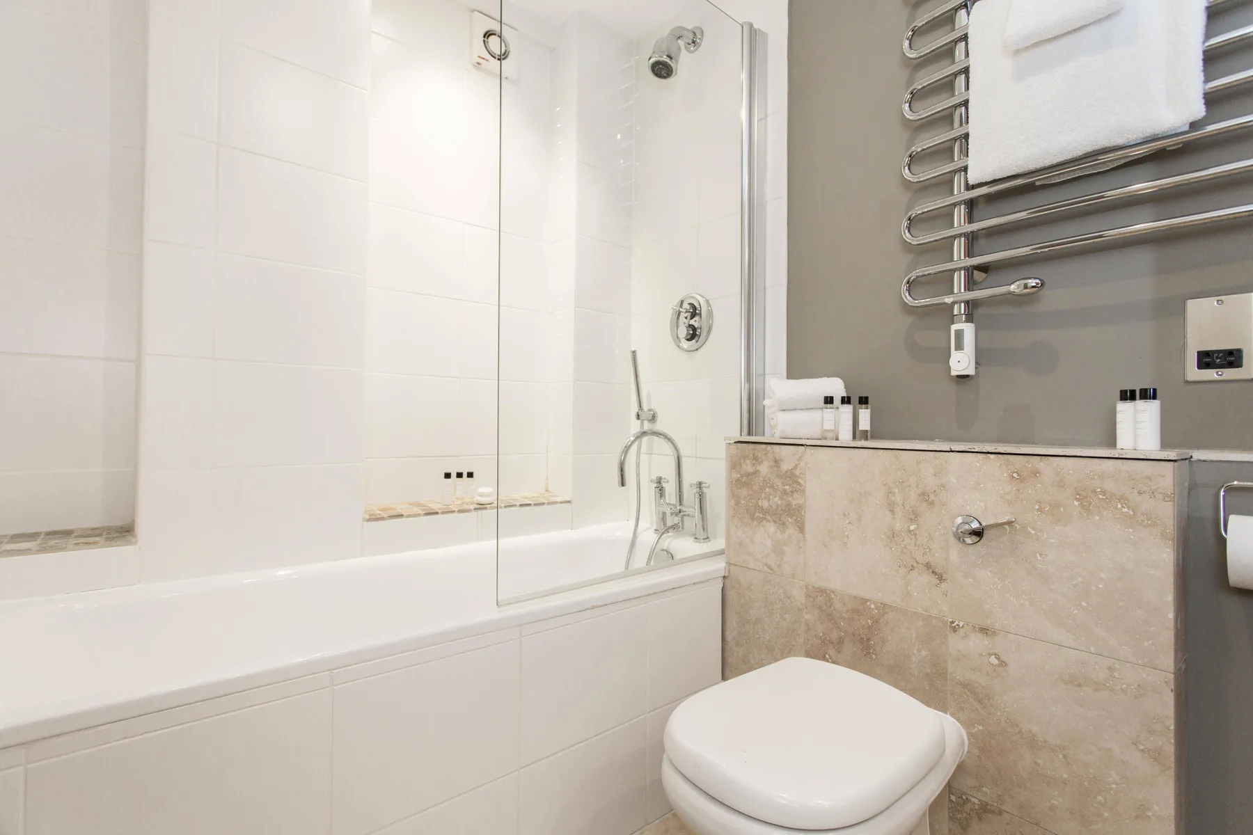 Un baño moderno con bañera, mampara de ducha de vidrio y toallero calefactable.