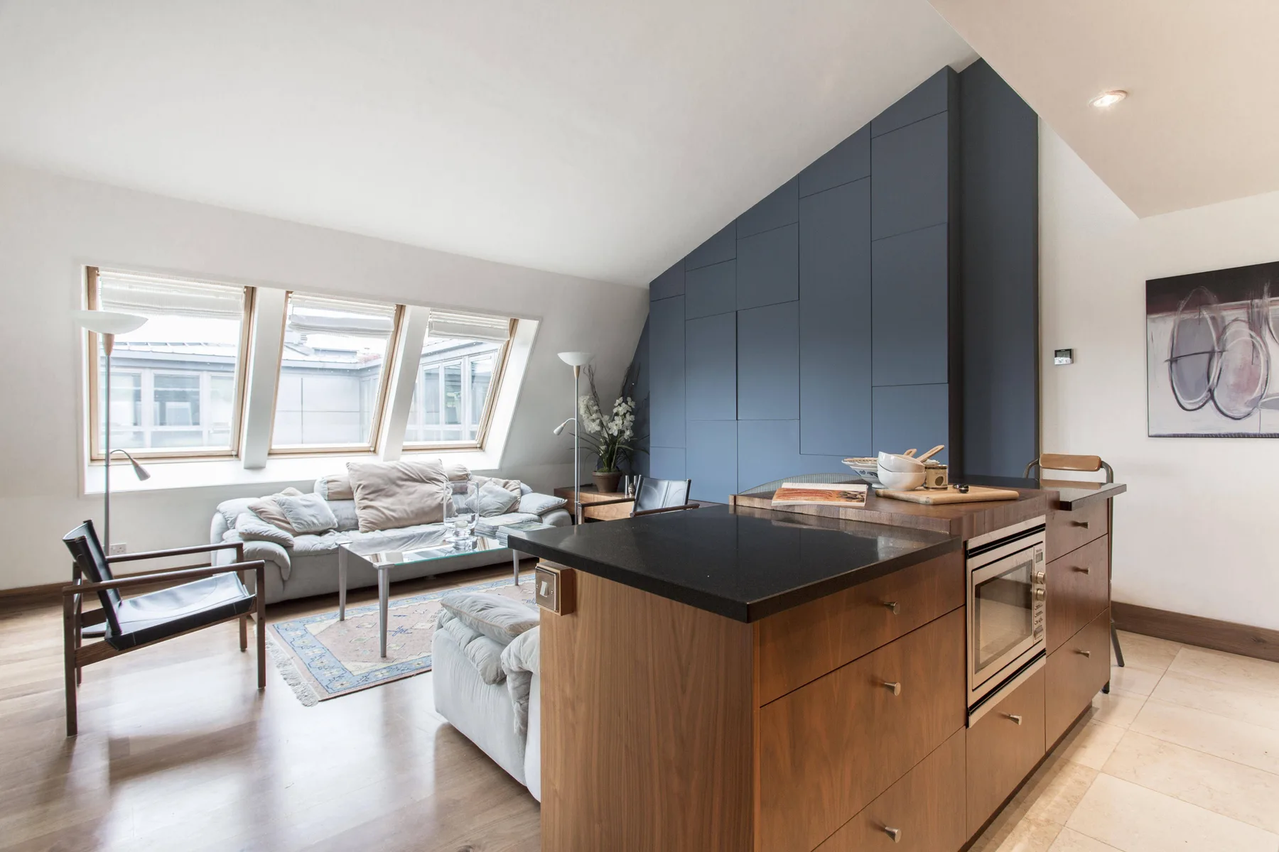 Un salón y cocina diáfanos y luminosos con grandes ventanas inclinadas.
