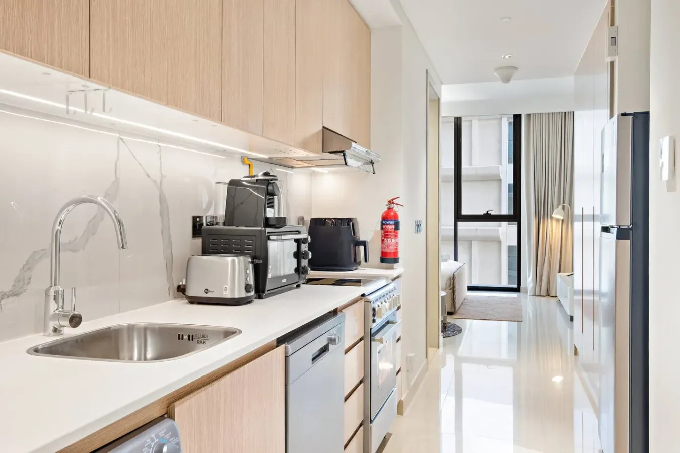 Una pequeña cocina luminosa da a un pasillo con ventanas grandes.