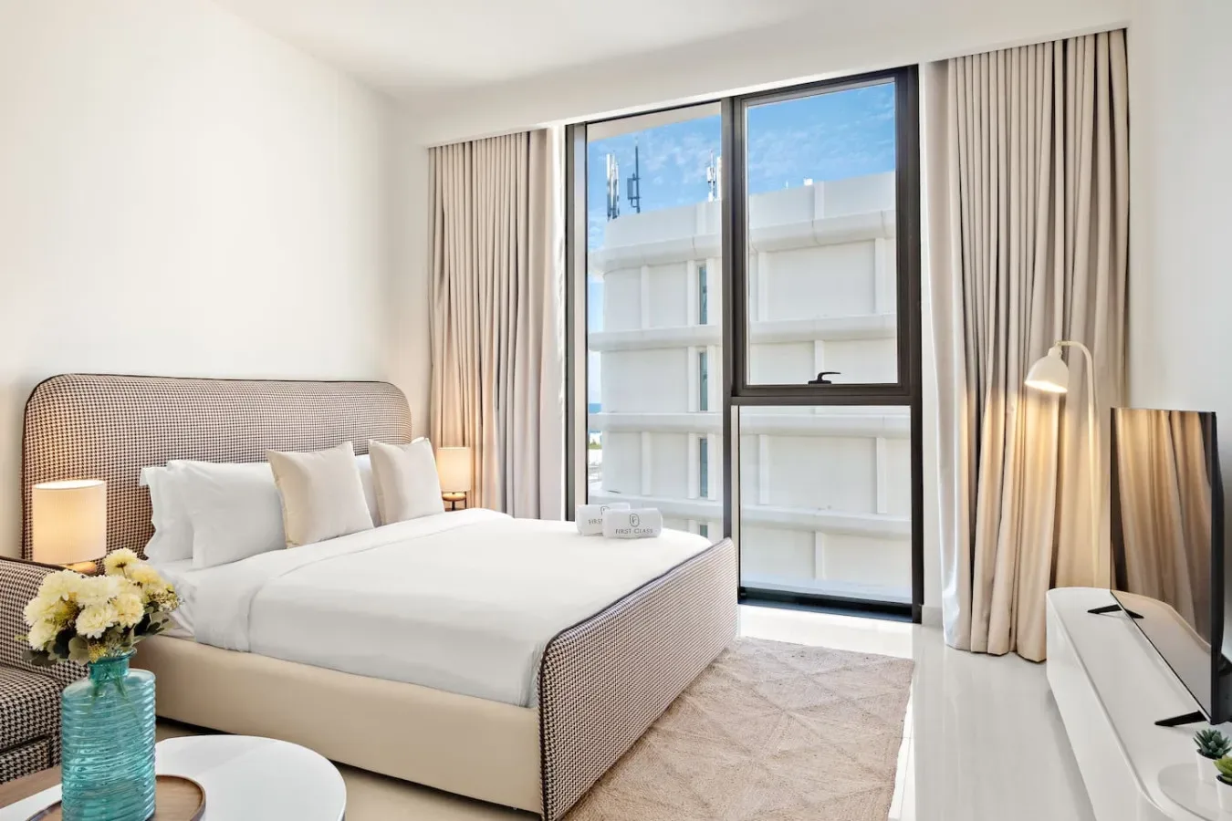 Un dormitorio luminoso con una cama tendida junto a una ventana grande.