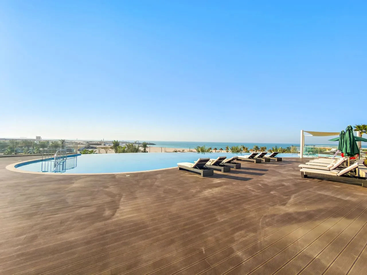 Una piscina en la azotea da al mar, con tumbonas junto a la terraza de madera.