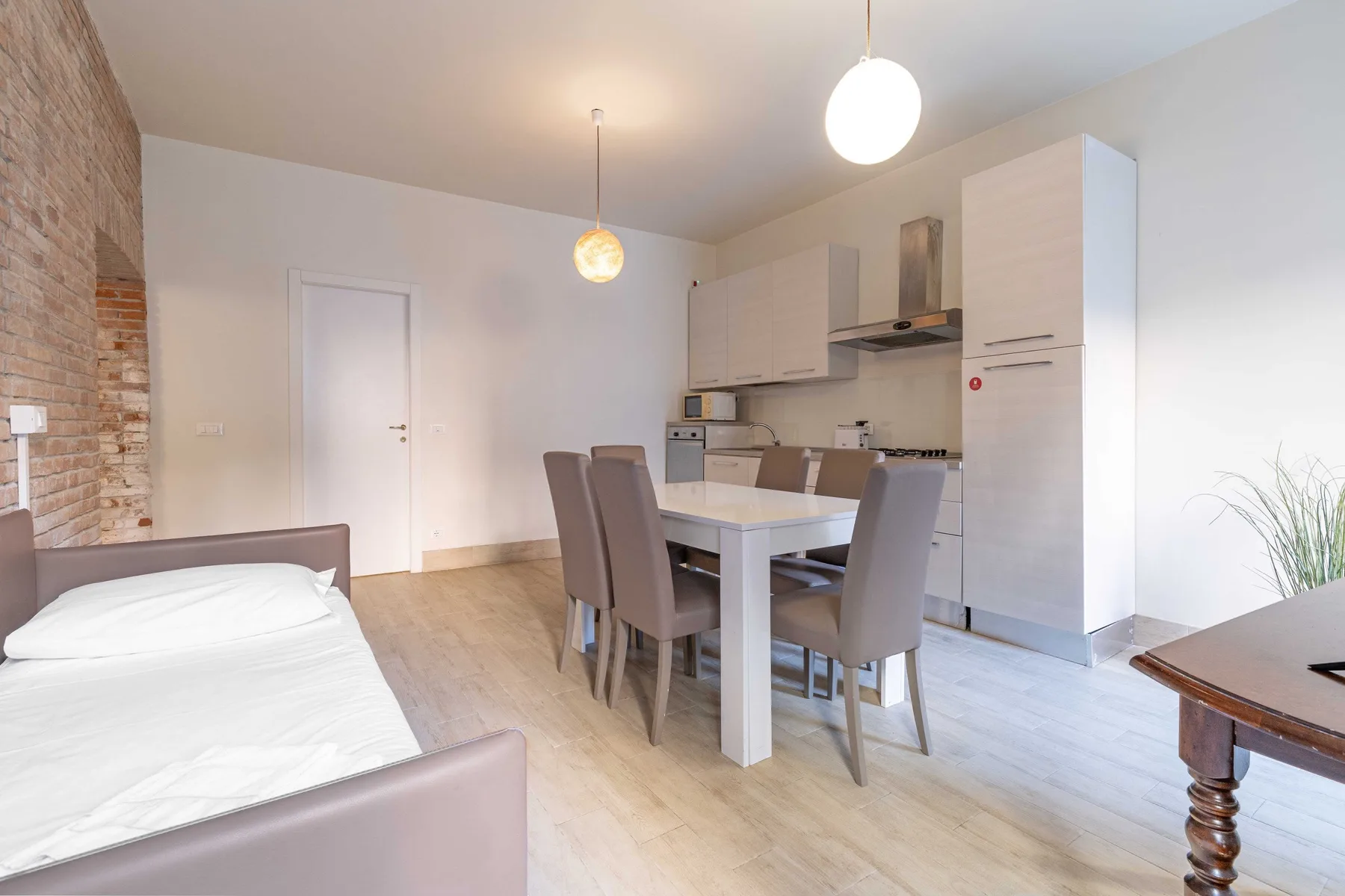 A bright bedroom and dining area with a bed, table, and kitchenette.
