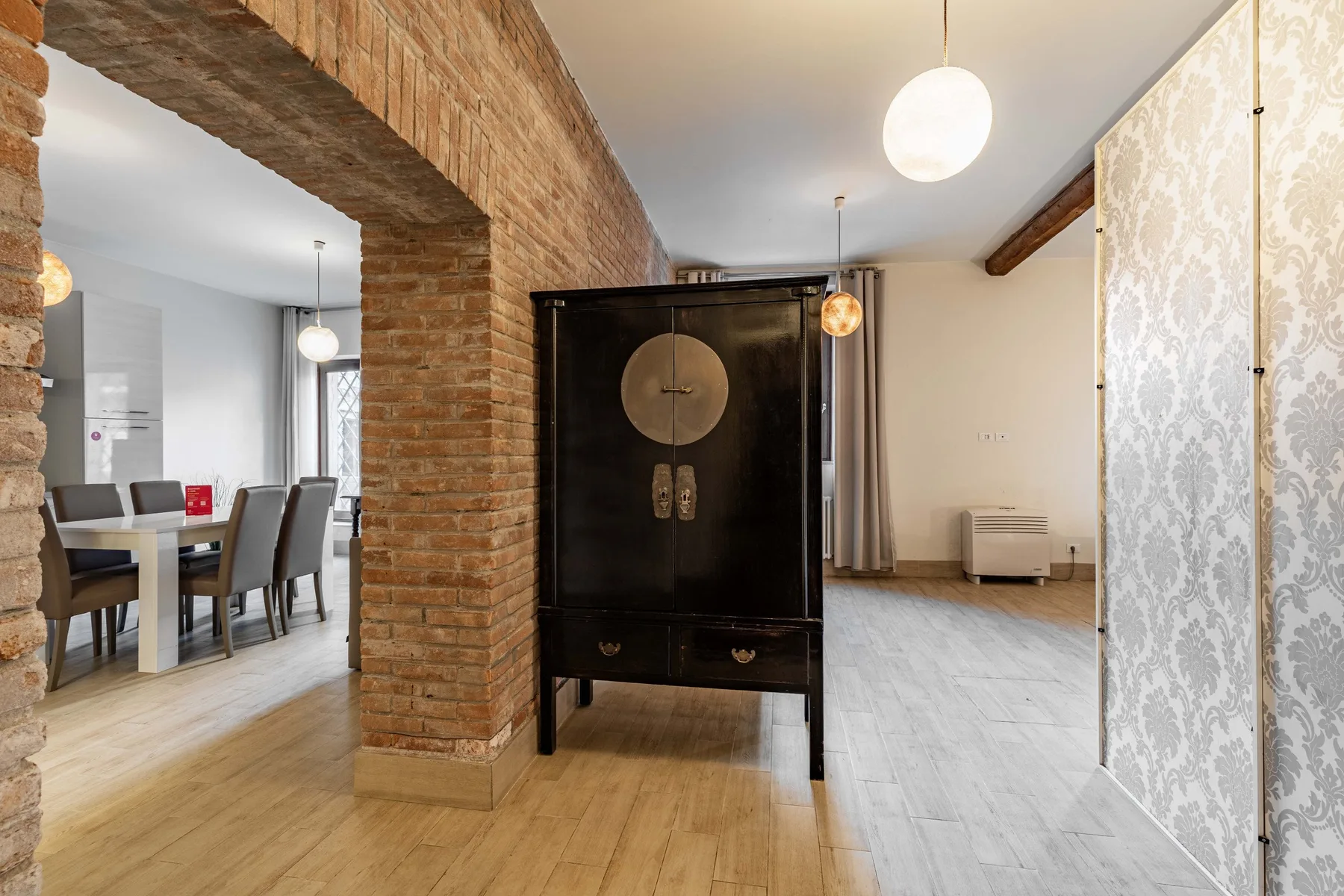Un comedor y una habitación contigua están separados por un arco de ladrillo y un mueble oscuro.