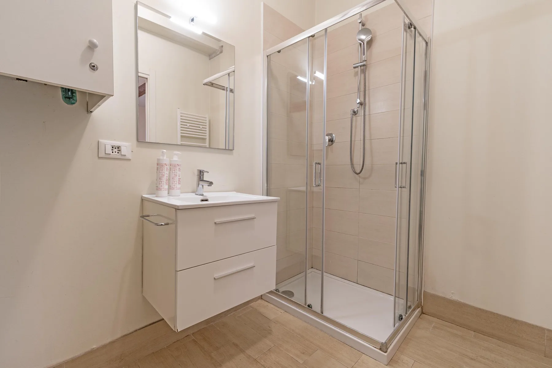 Un baño con una ducha de vidrio y un tocador suspendido.