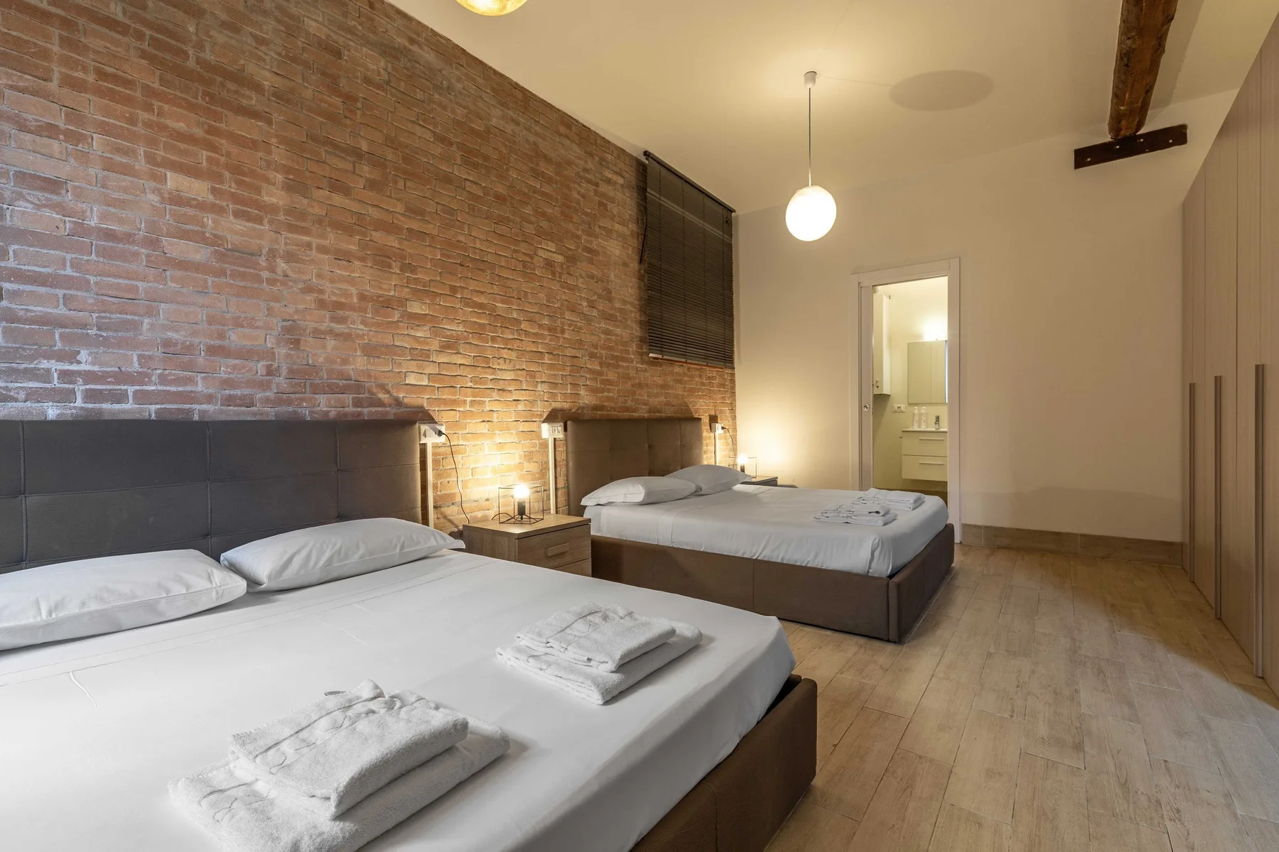 Un dormitorio con dos camas, paredes de ladrillo visto y suelo de madera.