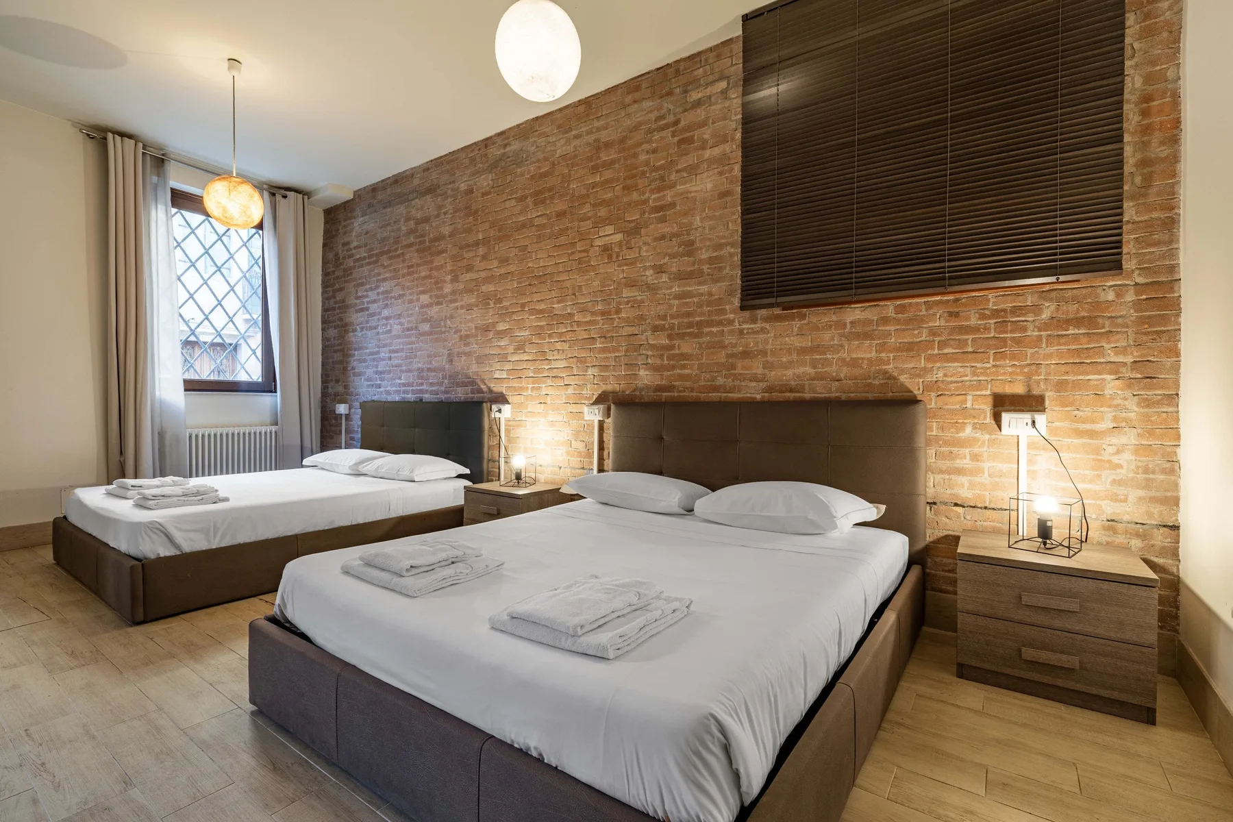 Un dormitorio con dos camas, mesitas de noche y una pared de ladrillo visto.