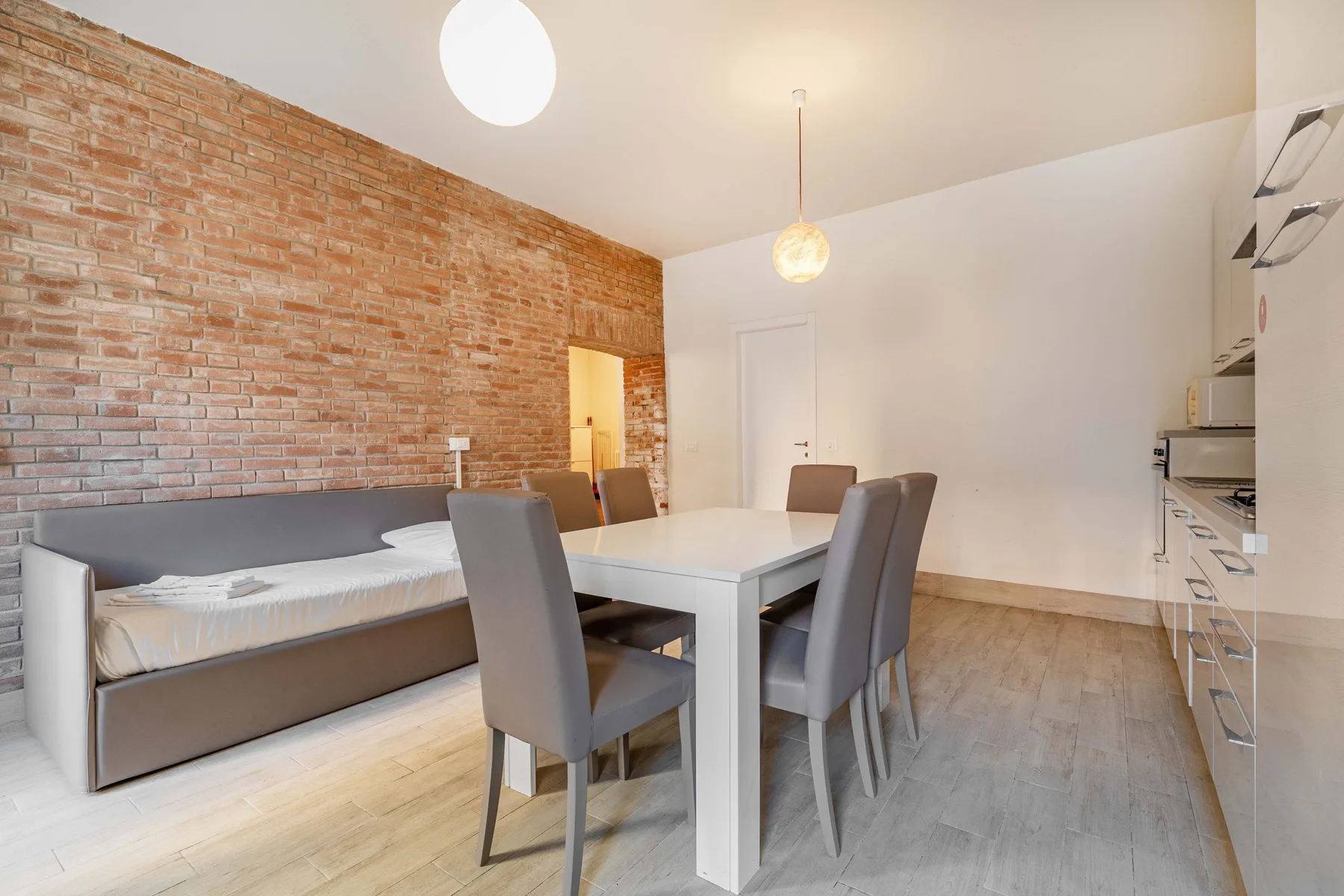 A dining area with a white table and gray seating beside a built-in bed.