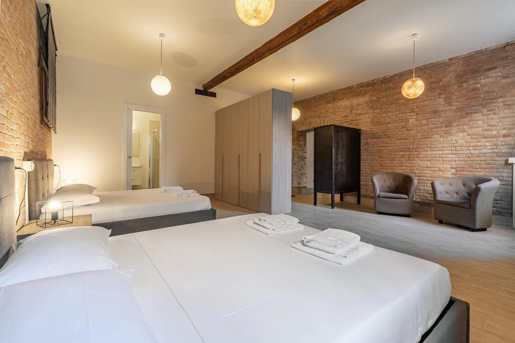 Un dormitorio con dos camas, paredes de ladrillo visto y un par de sillones.