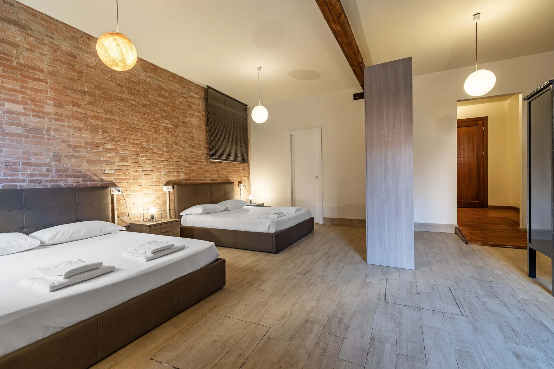 Un dormitorio con dos camas, una pared de ladrillo visto y suelo de madera.