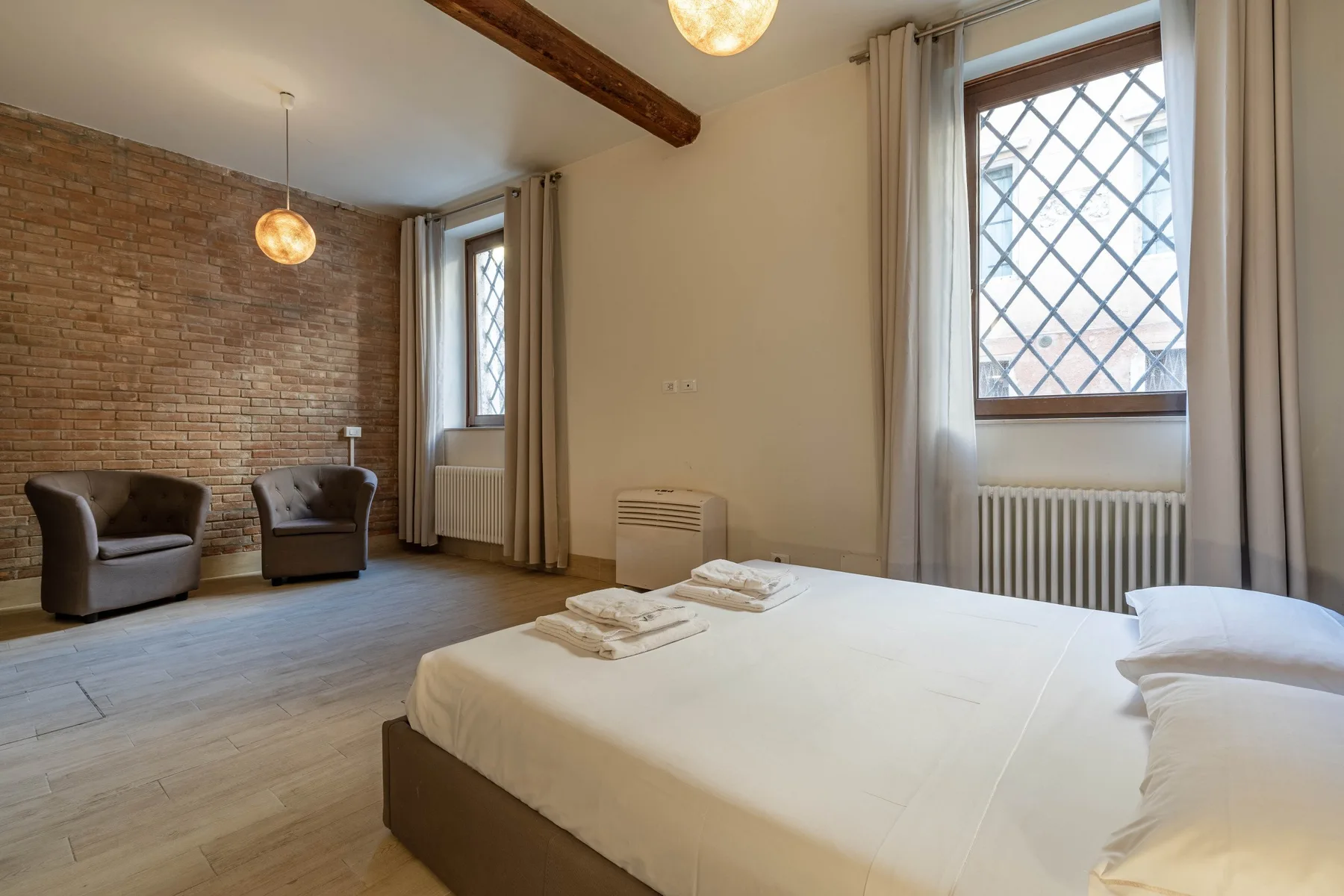 Un dormitorio con una cama grande y dos sillones junto a una pared de ladrillo.