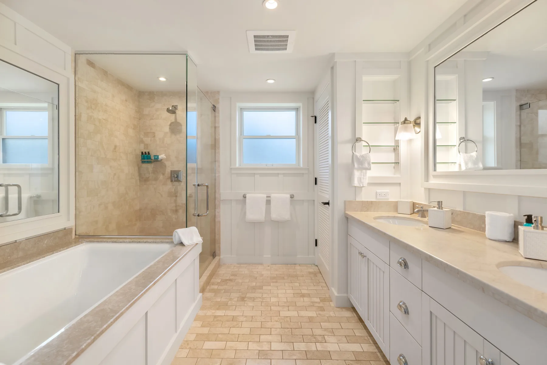 A bright bathroom with a bathtub, glass shower, and long vanity.