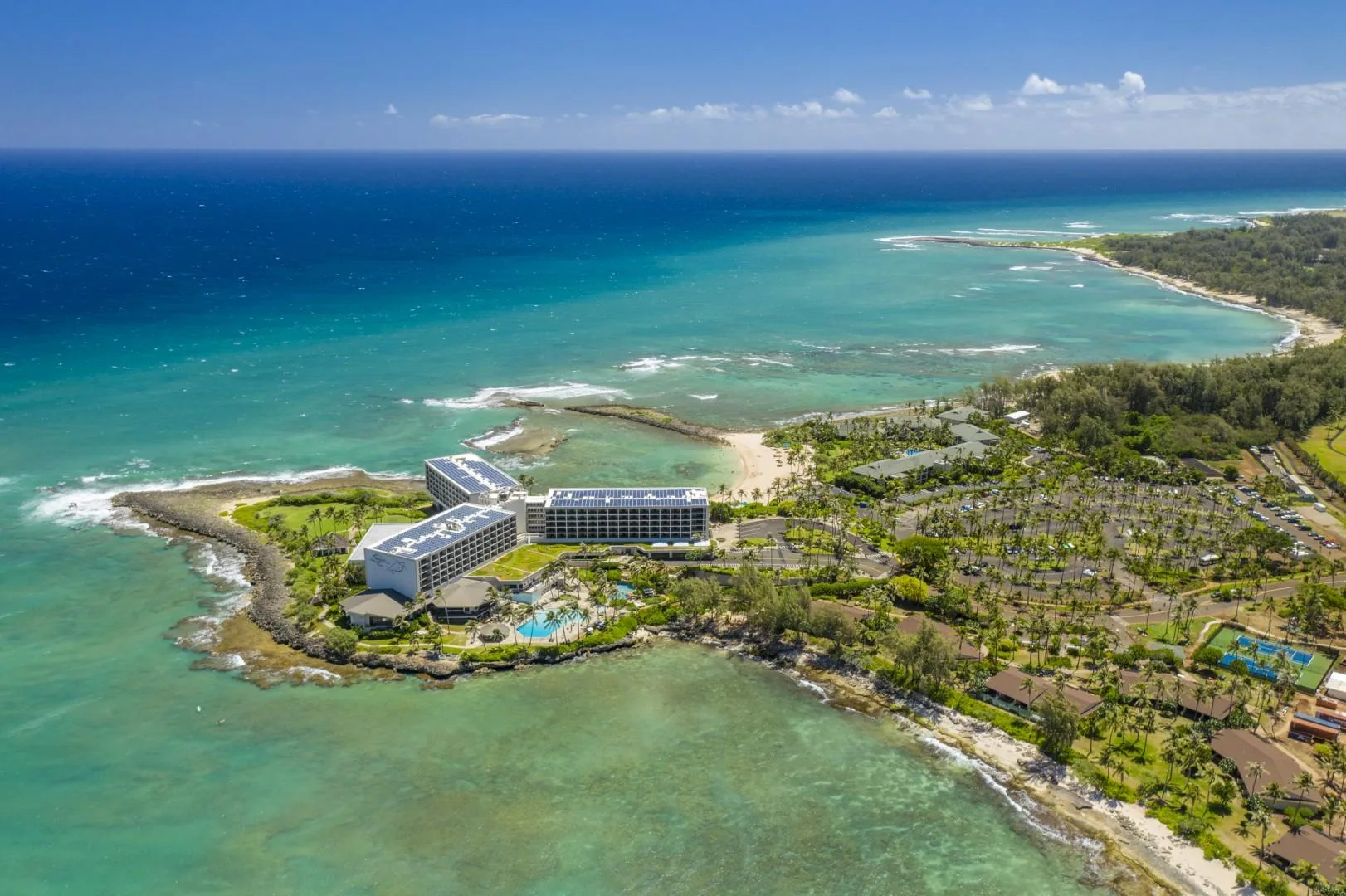 Aerial coastal view of a resort beside turquoise water and a sandy shoreline.
