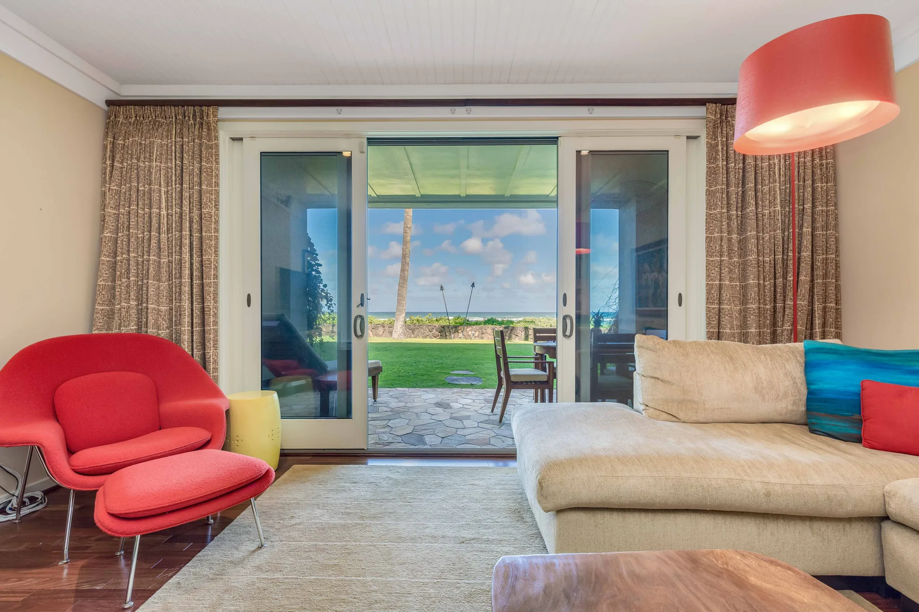 A living room opens through glass doors onto a garden and ocean view.