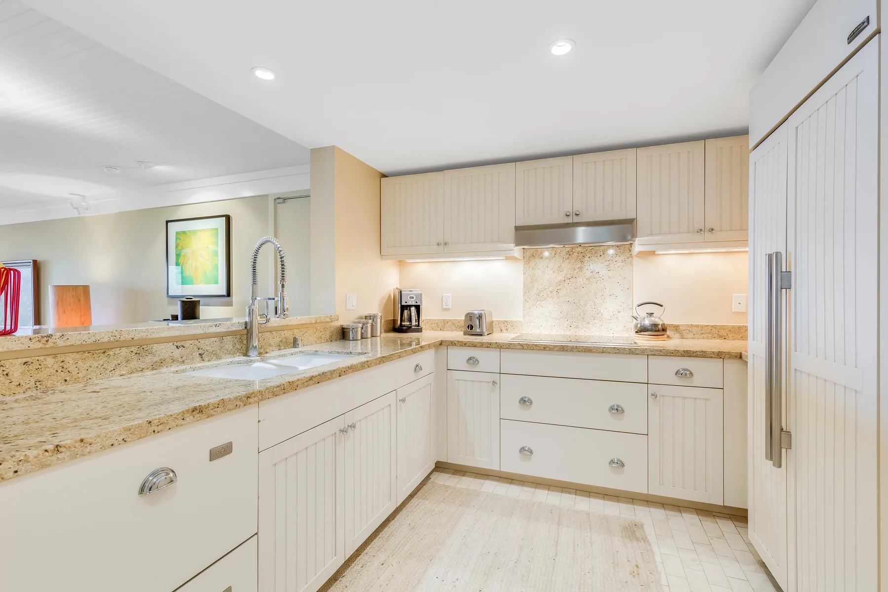 A bright kitchen with light cabinetry, stone counters, and a central cooking area.