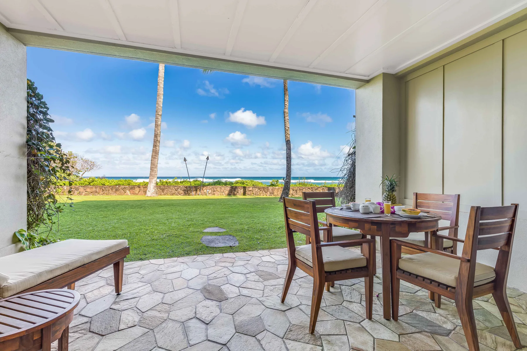 A covered outdoor dining area overlooks a green lawn and the ocean.