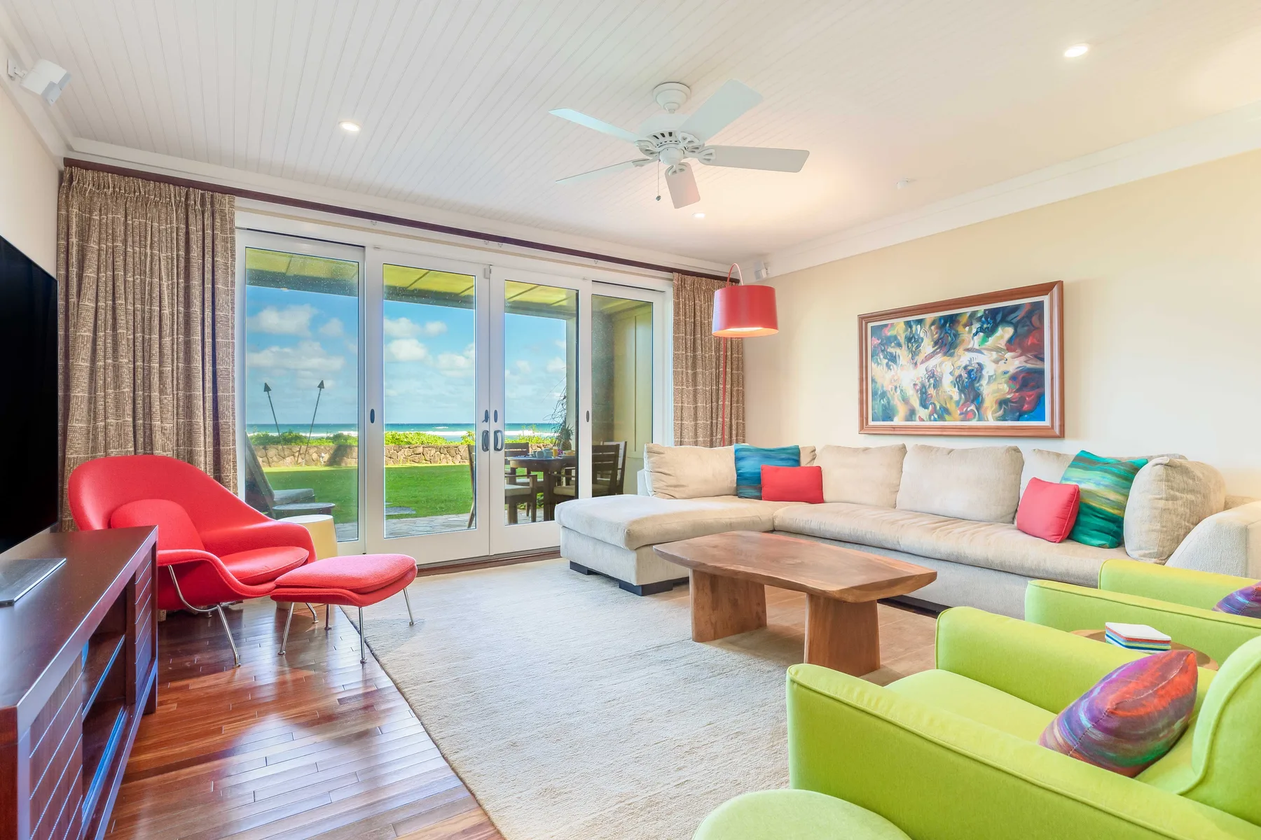 A bright living room with a sectional seating area and glass doors opening toward the ocean.