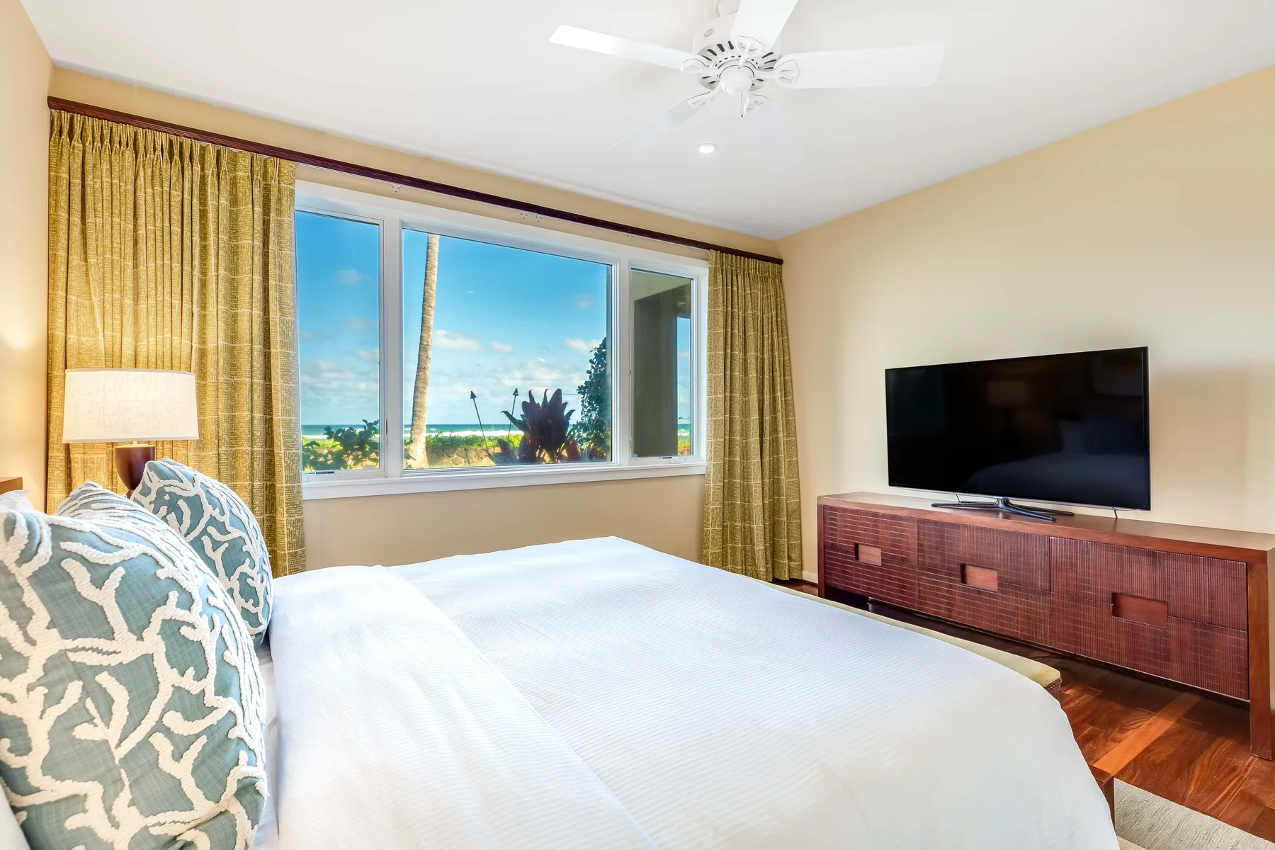 A bedroom with a bed, a window overlooking the ocean, and a television.