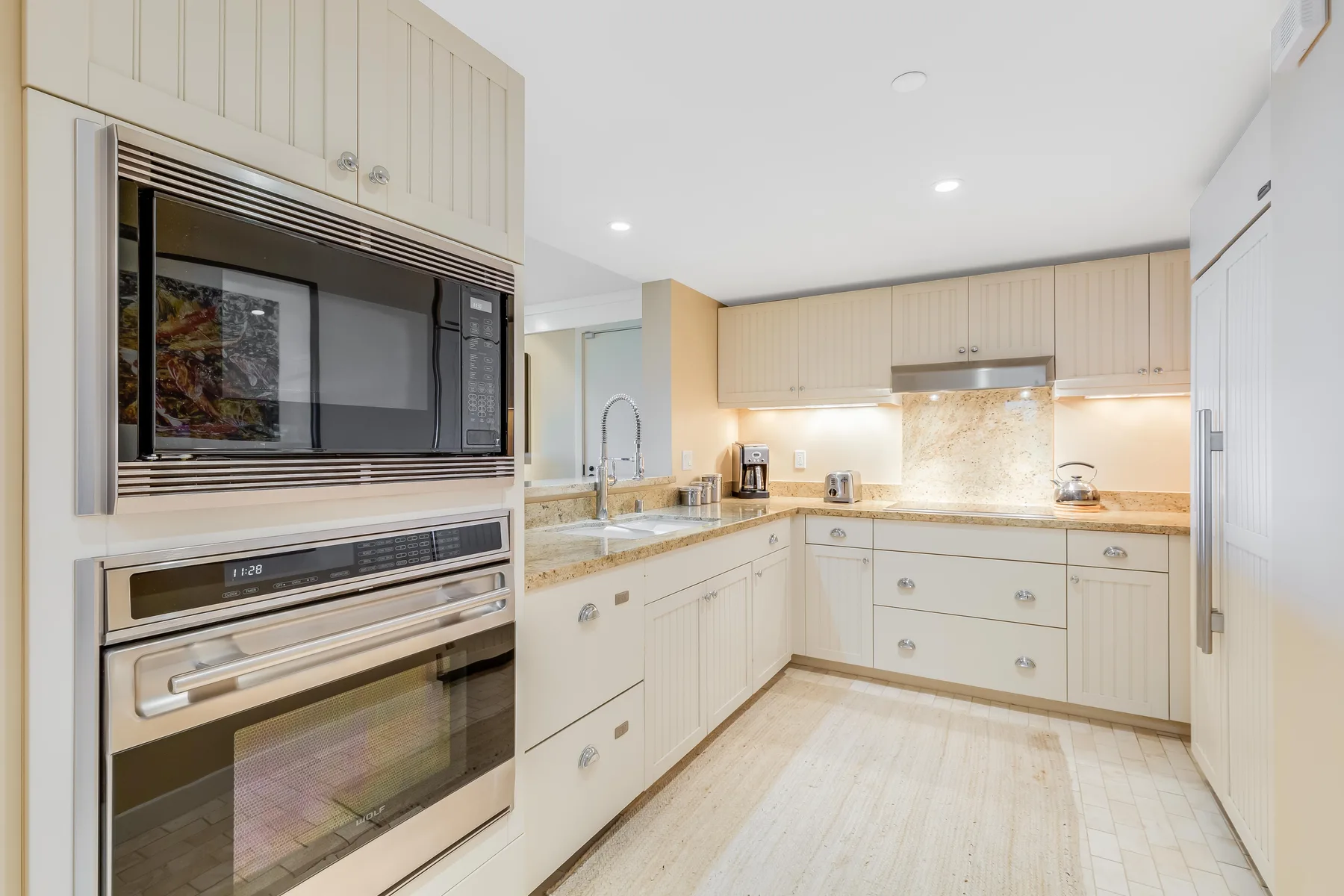 A bright kitchen with built-in appliances, pale cabinetry, and a central countertop.
