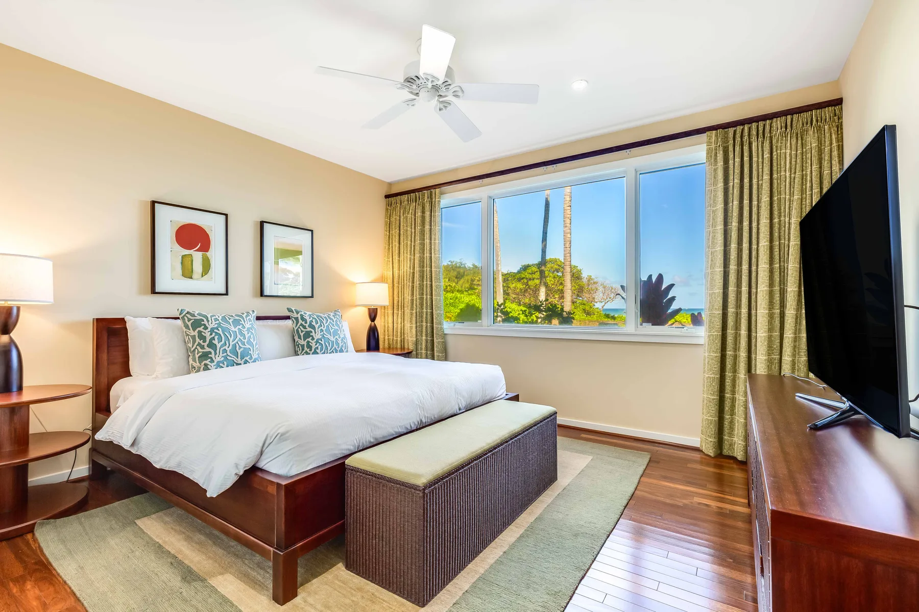 A bedroom with a large bed, broad windows, and a television.
