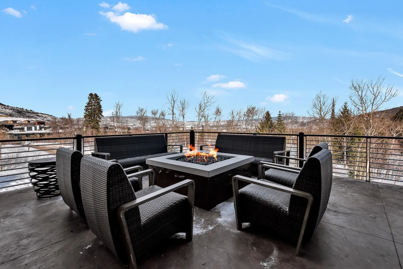 An outdoor patio seating area surrounds a square fire pit beneath an open sky.