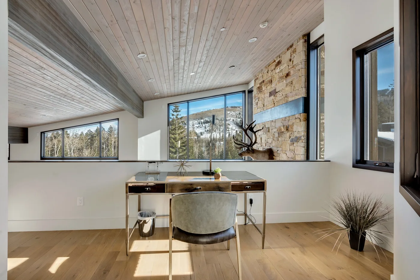 A bright workspace with a desk and chair sits beside large windows and a stone accent wall.
