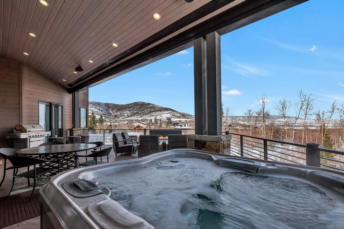 A covered outdoor seating area overlooks a snowy landscape beside a bubbling hot tub.