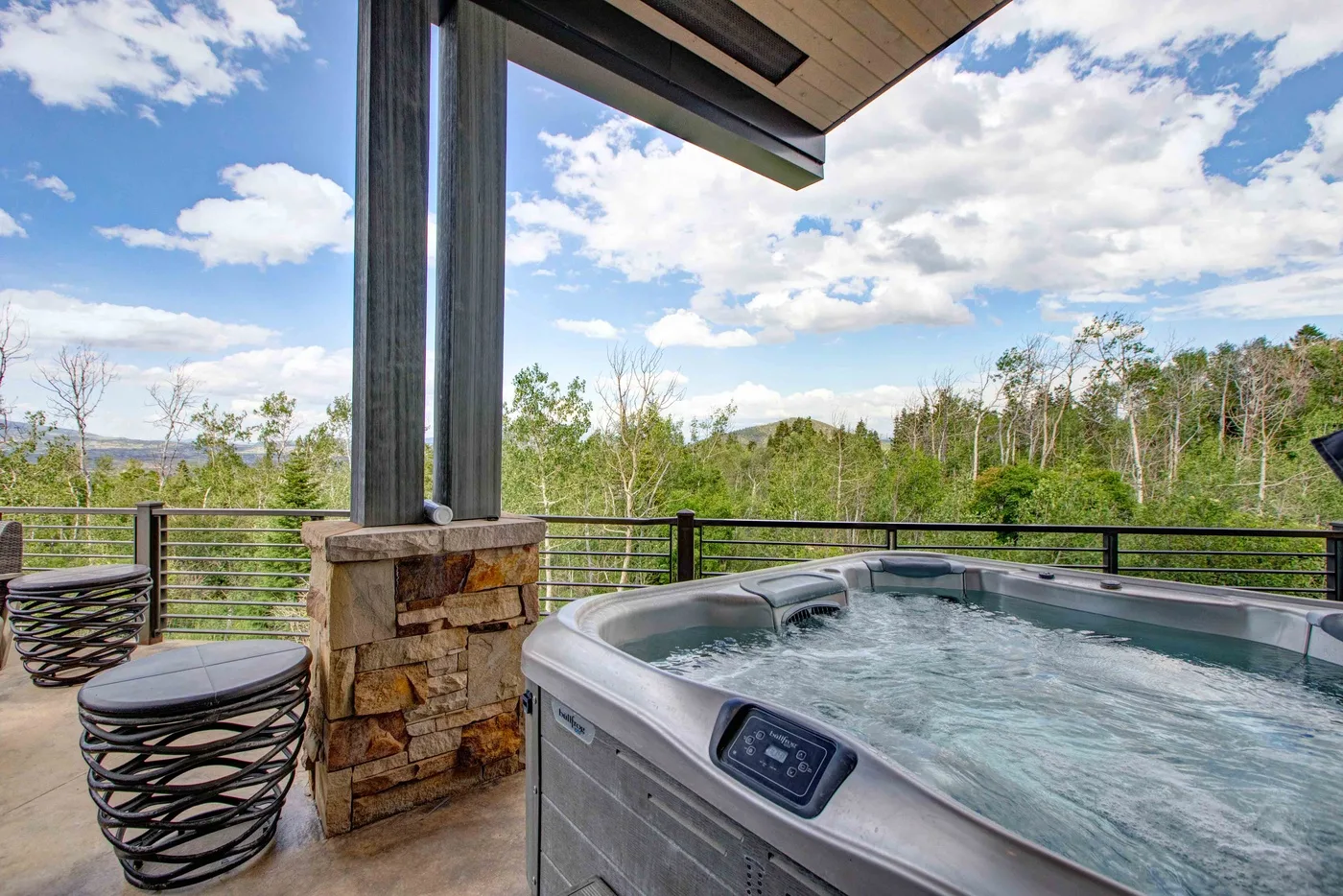 A bubbling hot tub sits on a covered deck overlooking a wooded landscape.