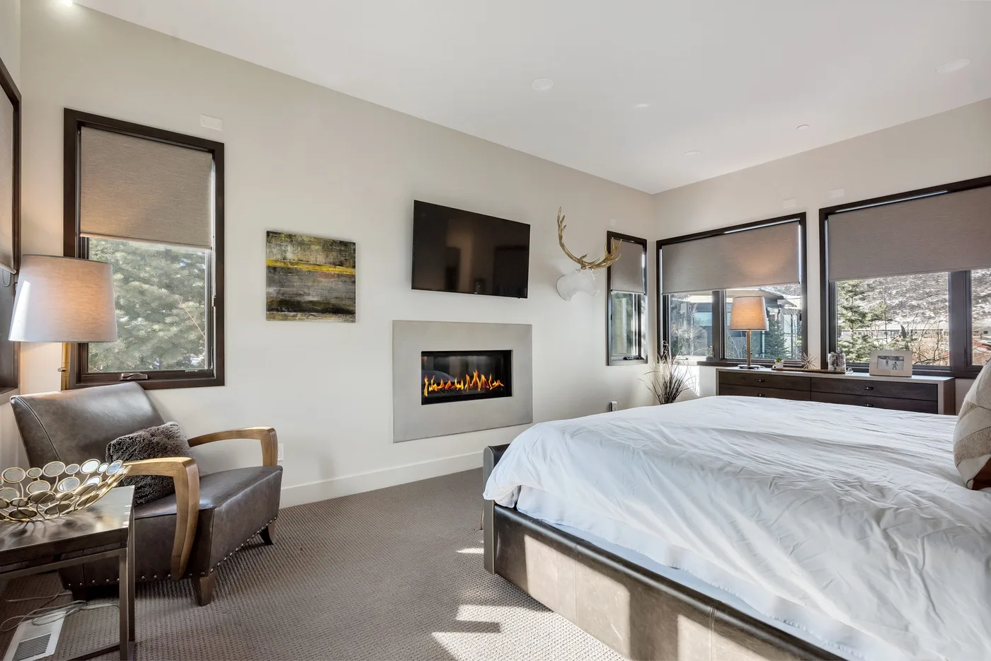 A bedroom with a large bed, a fireplace, and windows overlooking the landscape.