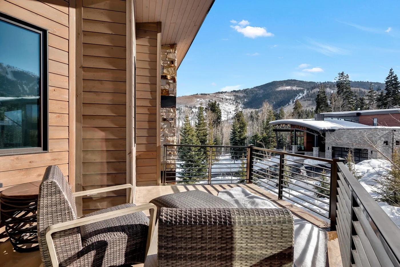 A wooden deck with woven seating overlooks a snowy mountain landscape.