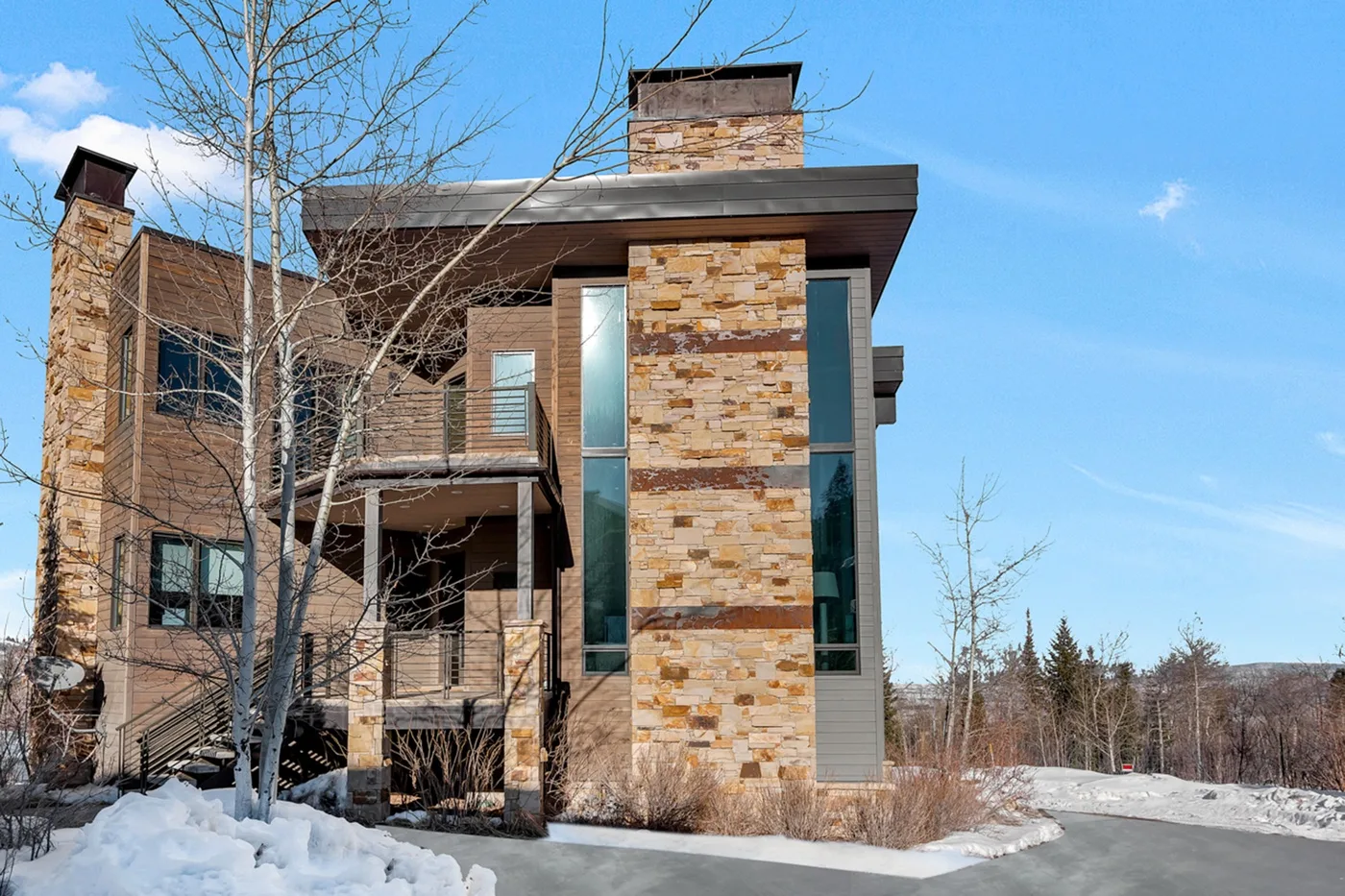 A modern multi-story house with stone accents stands beside a snowy driveway.