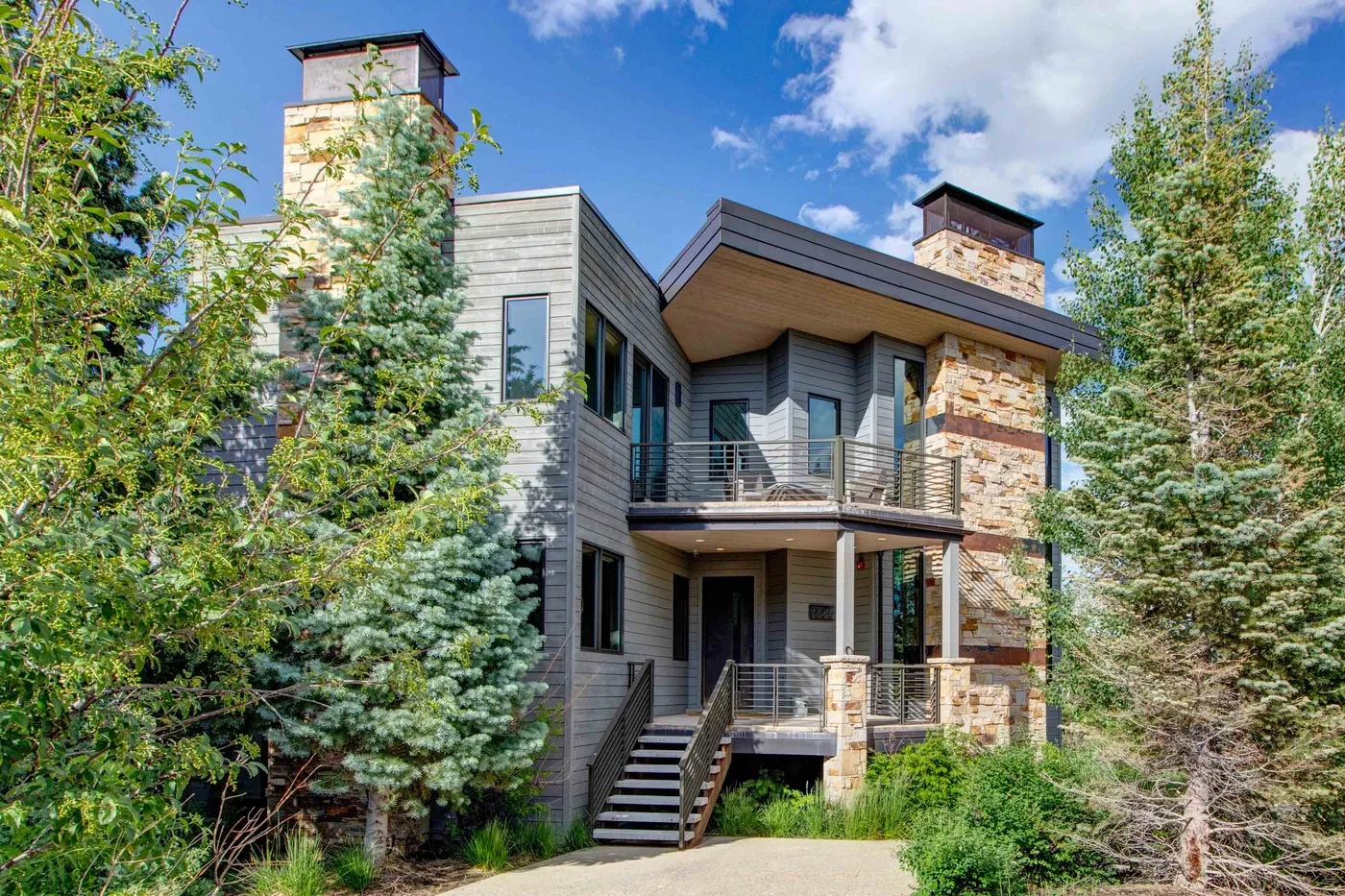 A modern house with stone chimneys and balconies surrounded by trees.