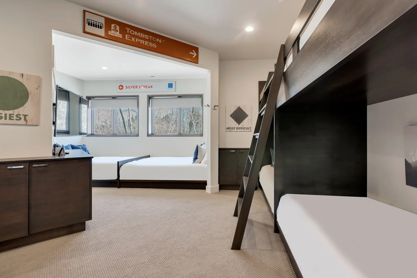A bedroom with several beds, windows, and a dark bunk bed in the foreground.