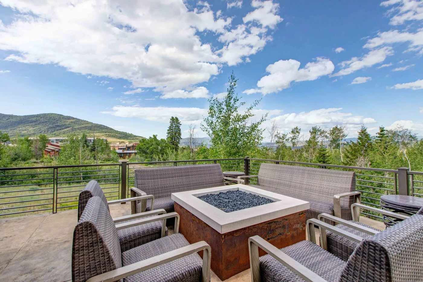 An outdoor seating area with a square fire pit overlooks a green landscape.
