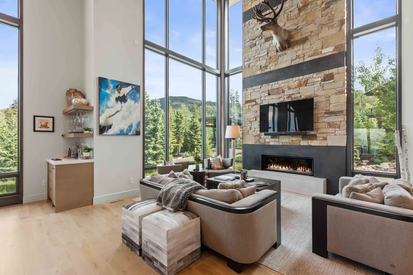 A bright living room with large windows, seating, and a stone fireplace.