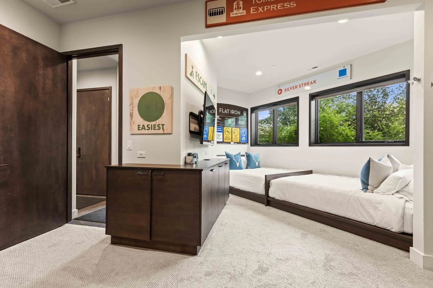 A bright bedroom with two beds, a dark wood counter, and large windows.