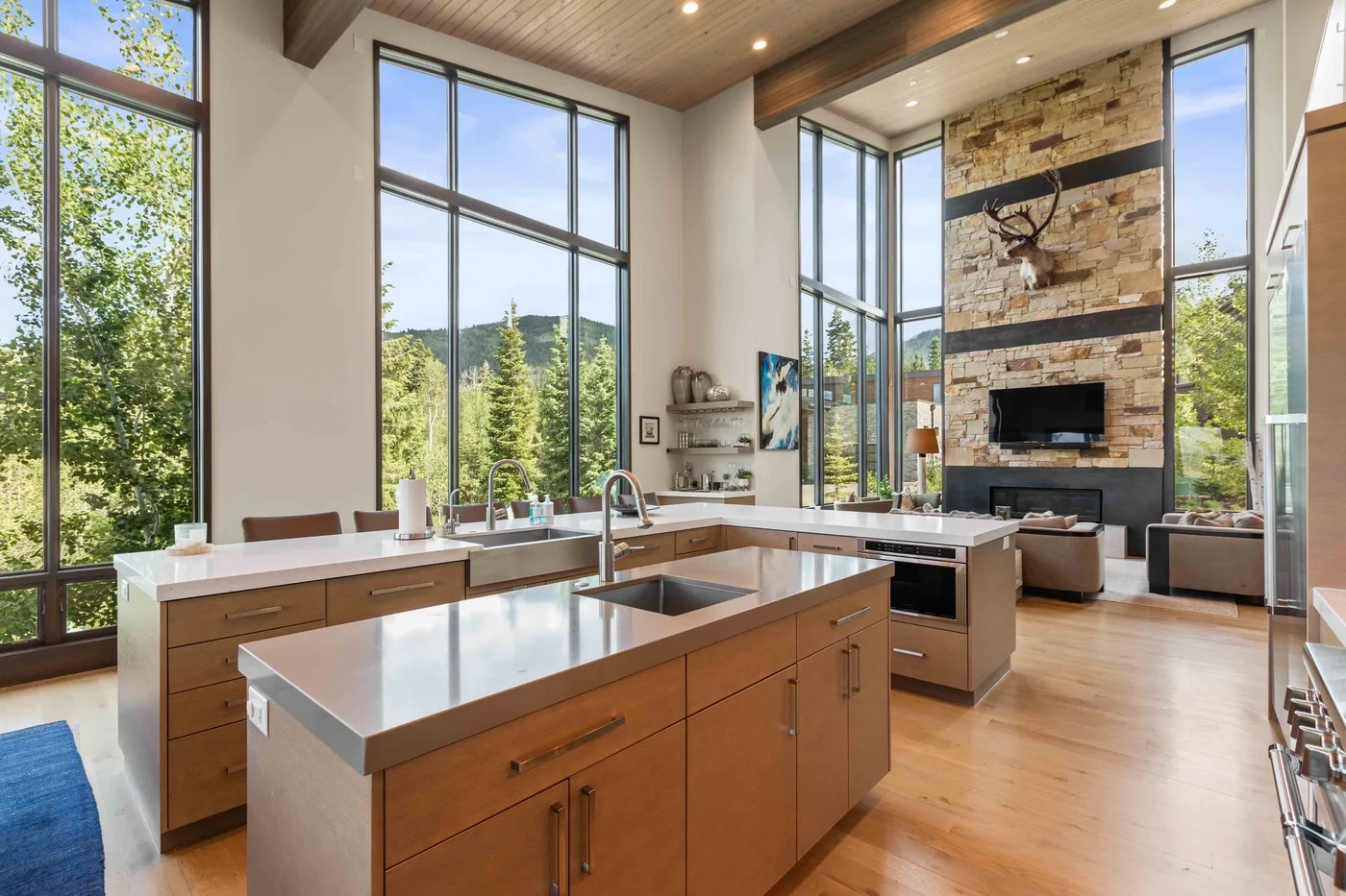 A bright open-plan kitchen and living area with large windows and a stone fireplace.