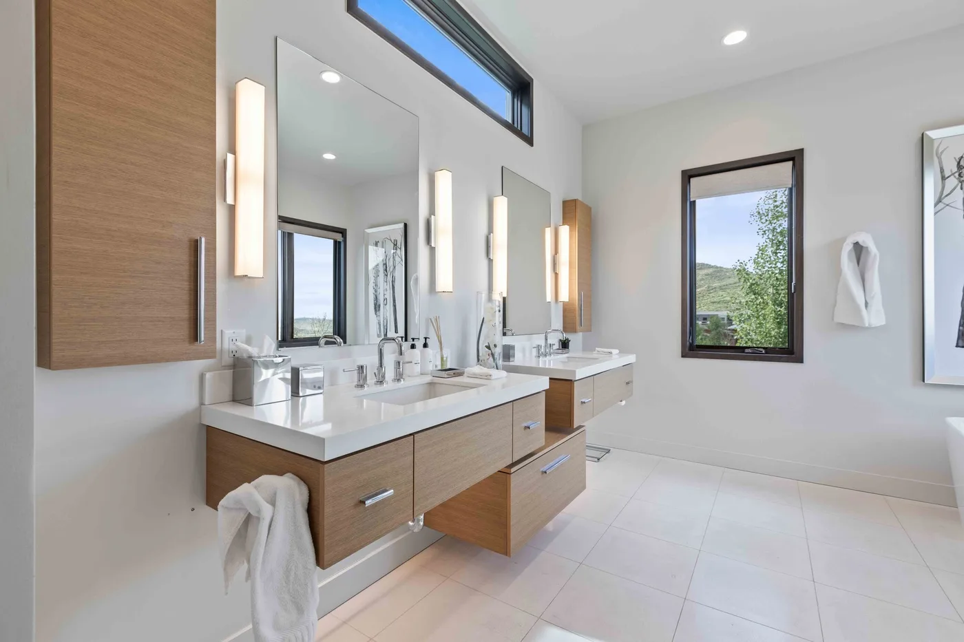 A bright bathroom with a long vanity, mirrors, and a large window.