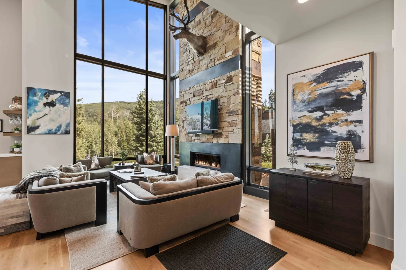 A bright living room with large windows, seating, and a stone fireplace.