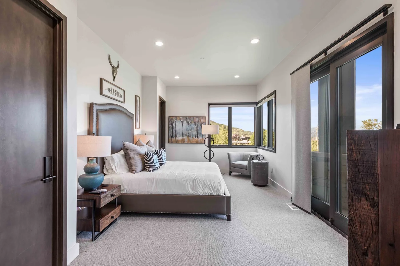 A bright bedroom with a bed, bedside tables, and large windows.
