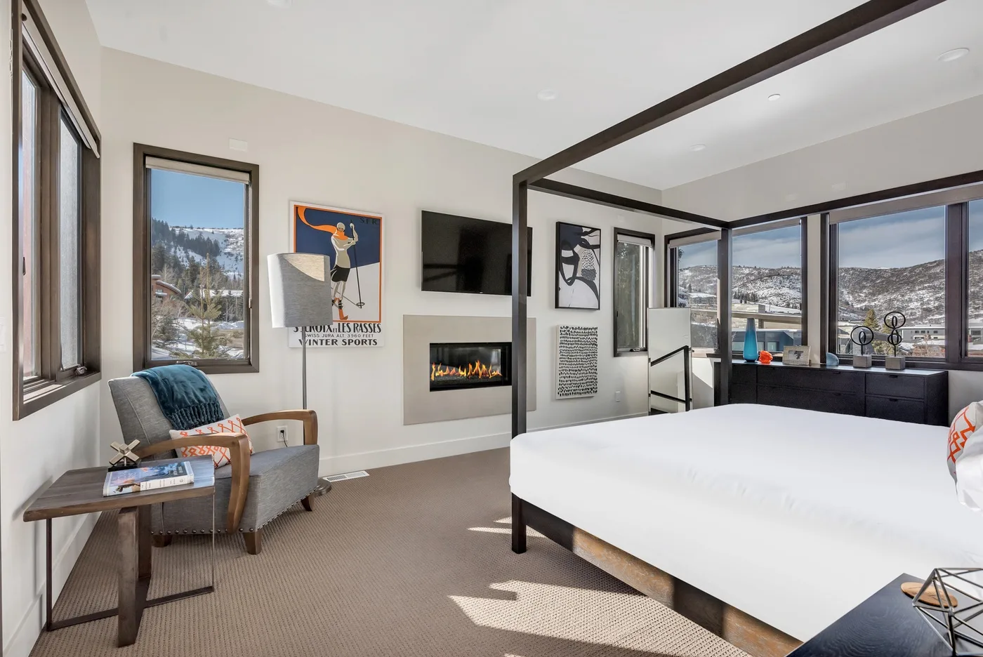 A bright bedroom with a large bed, a television, and windows overlooking a snowy landscape.