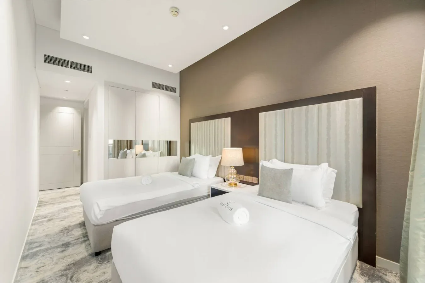 A bright bedroom with two beds and a bedside lamp.