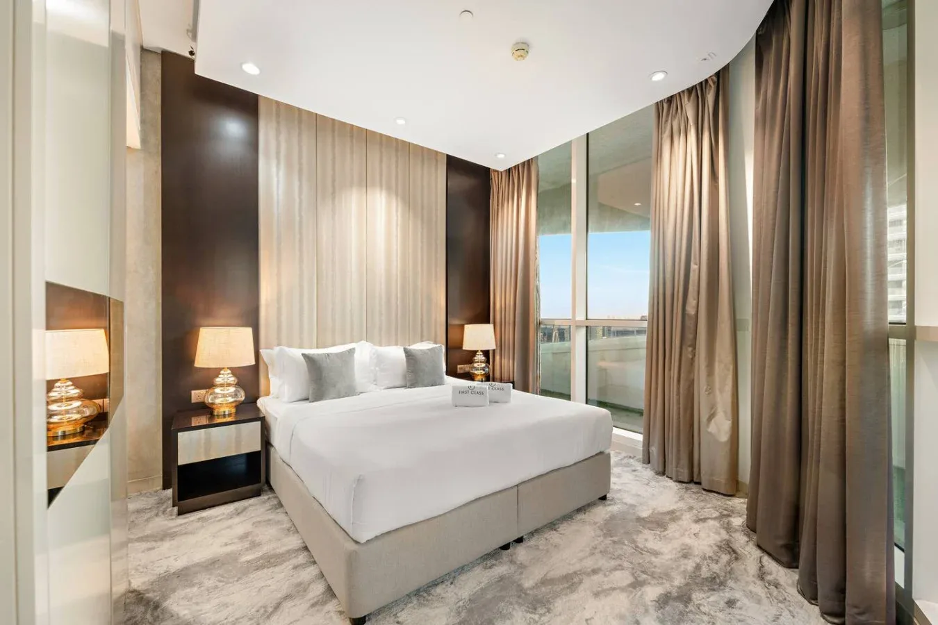 A bedroom with a bed beside floor-to-ceiling windows and curtains.