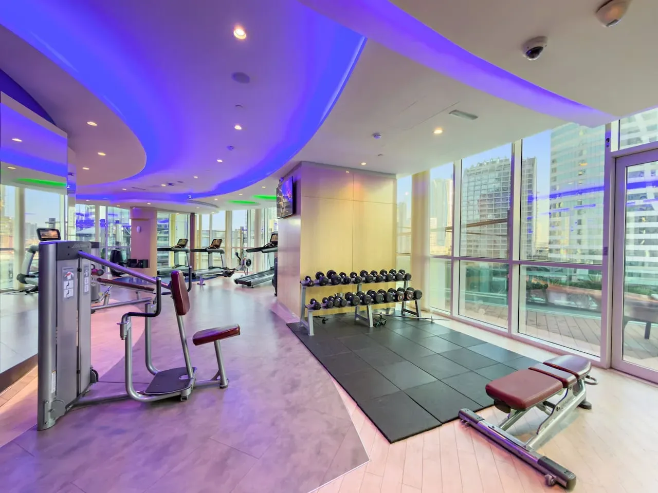 A gym with exercise machines, weights, and large windows.