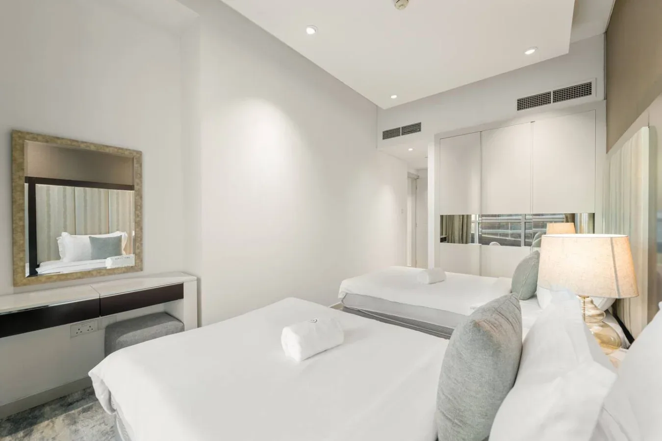 A bright bedroom with white bedding, bedside seating, and a wall mirror.