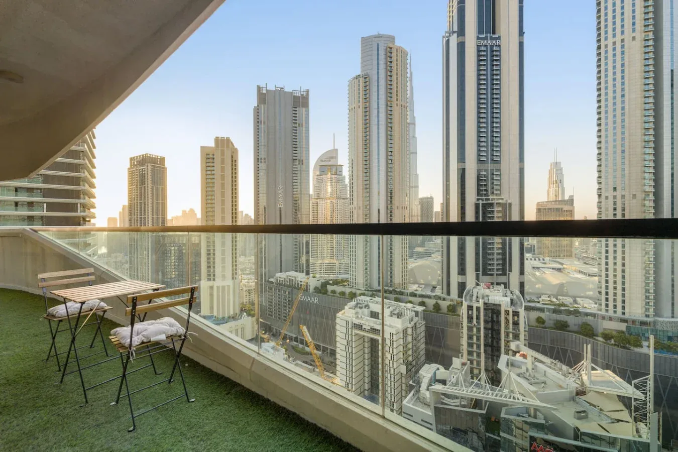 A balcony with a small table and seating overlooks a skyline of tall buildings.