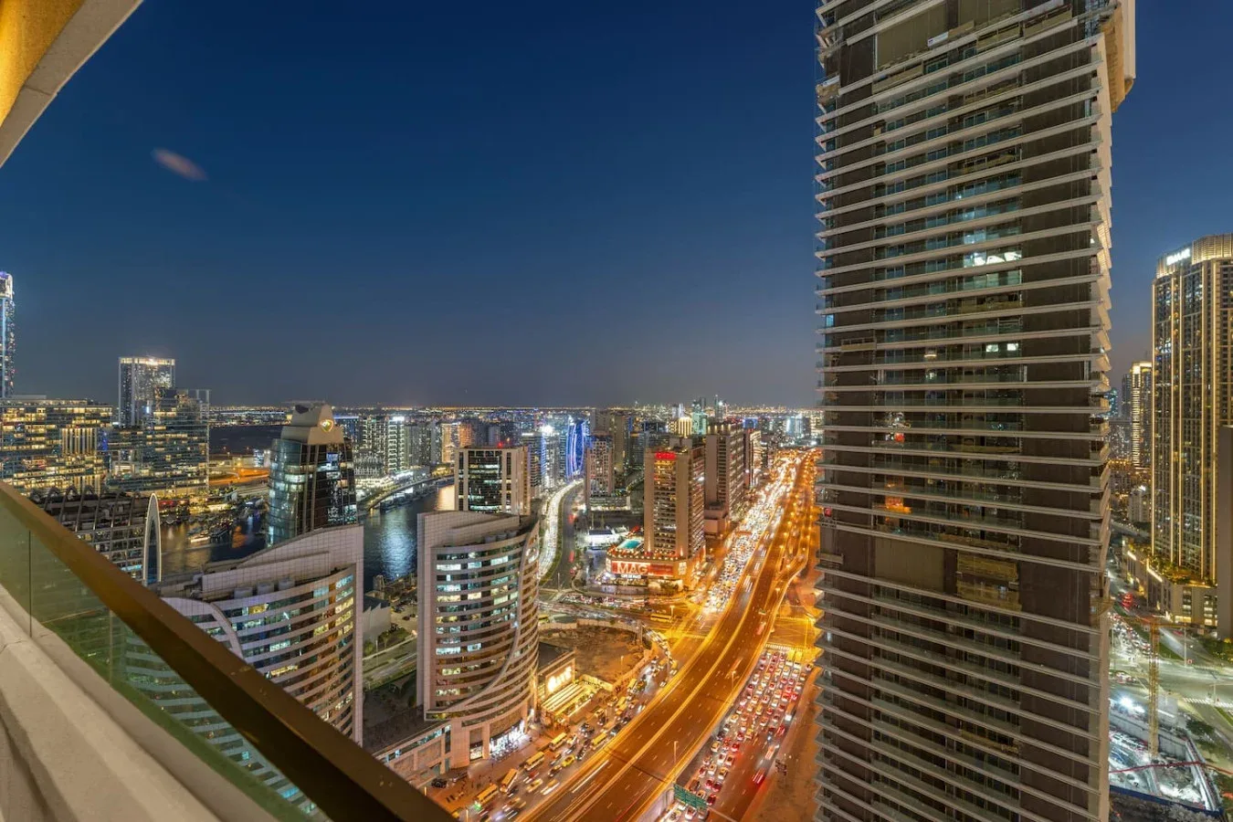 A nighttime city skyline viewed from a balcony, with brightly lit roads below.