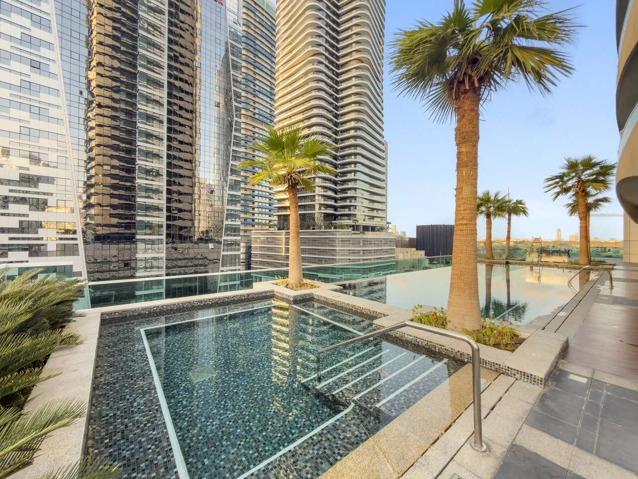 Outdoor swimming pool beside modern high-rise buildings and palm trees.
