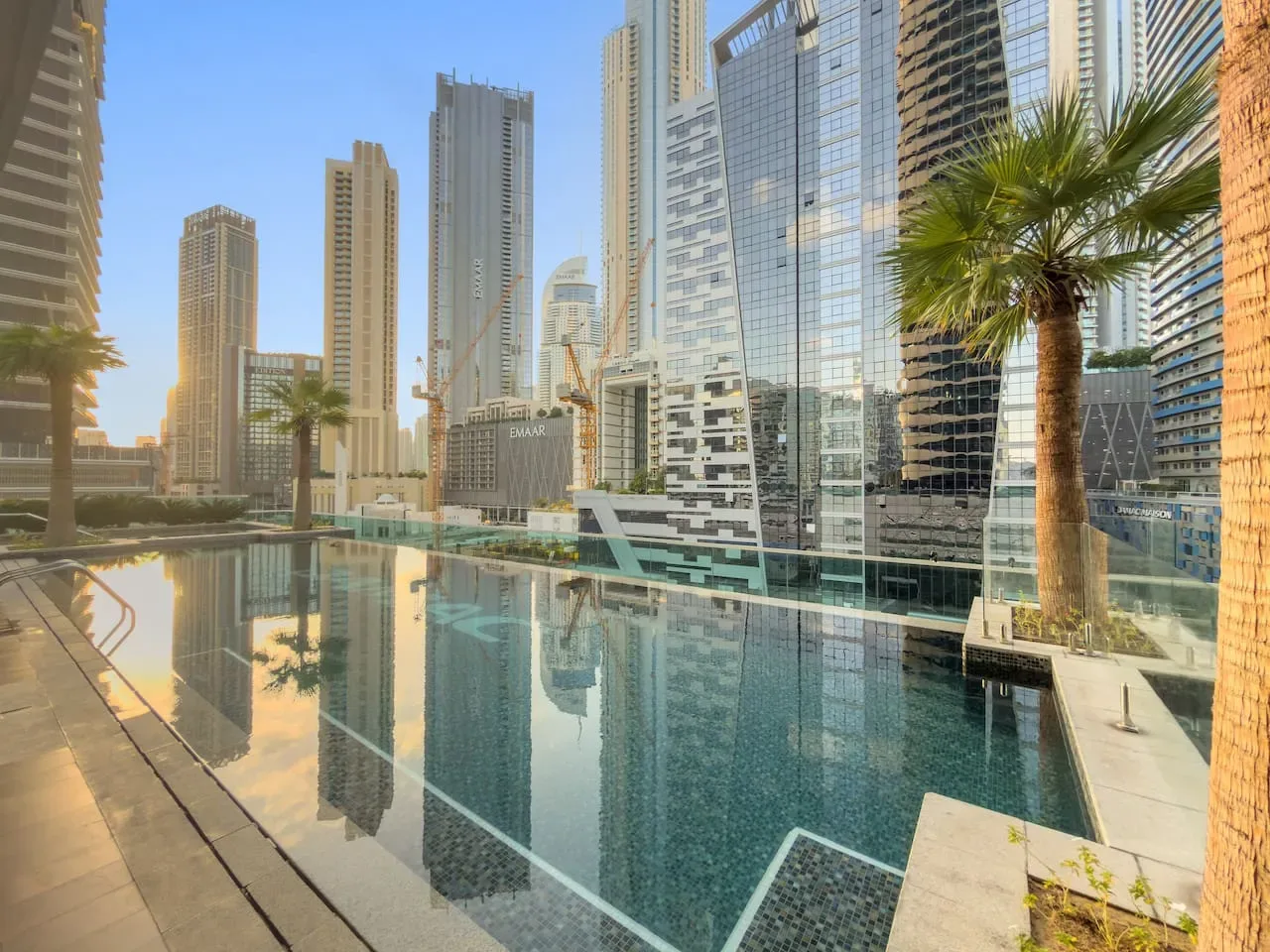 A swimming pool reflects the surrounding high-rise buildings in a modern urban setting.