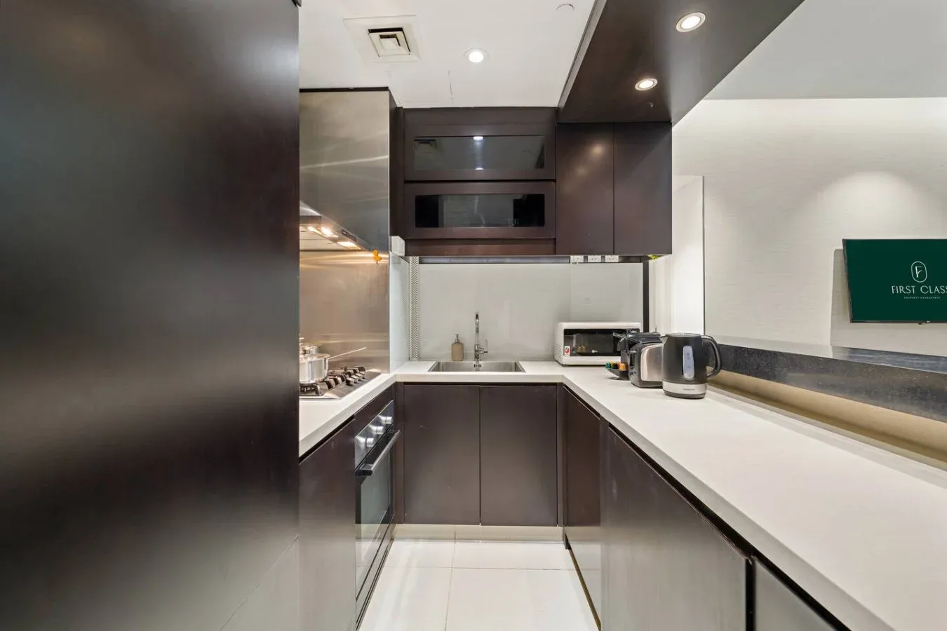 A modern kitchen with dark cabinets, a sink, and long white countertops.