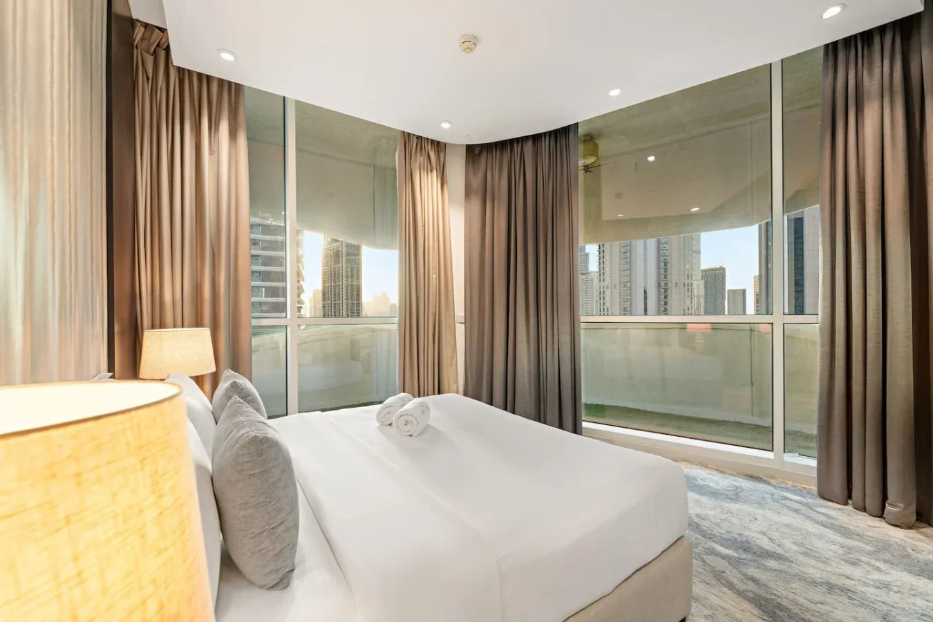 A bedroom with a bed beside floor-to-ceiling windows and curtains.